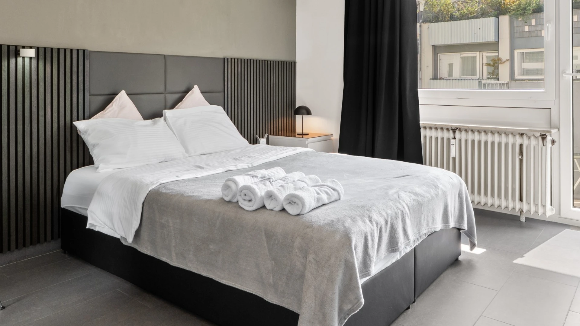 Modernes Schlafzimmer mit Doppelbett und dunklem Lamellenkopfteil im Cozy Cologne Rentals Apartment am Neumarkt in Köln.