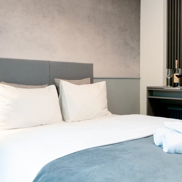 Helles Doppelbett mit grauem Kopfteil und strukturierter Wand in einem Cozy Cologne Rentals Apartment im Zentrum von Köln.